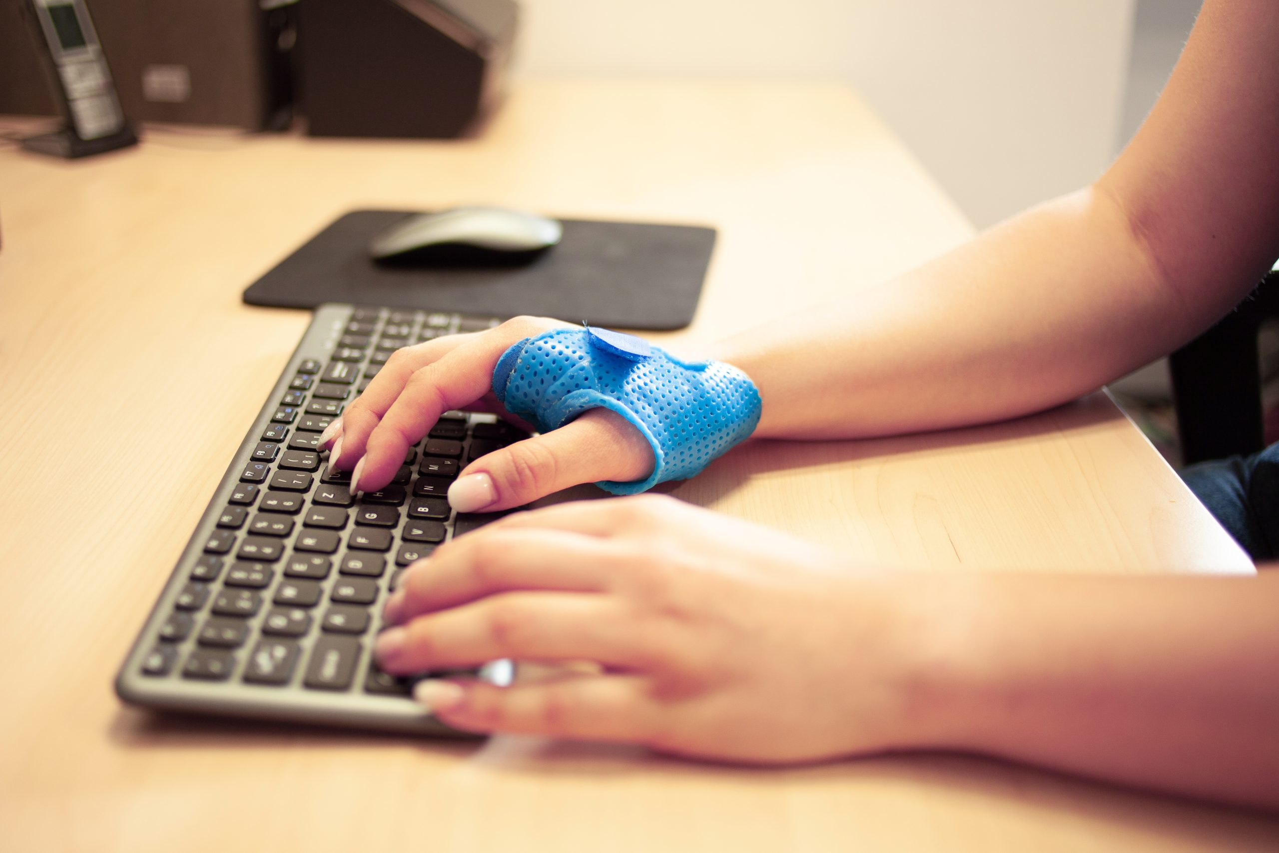 Person, die auf einer Tastatur tippt, trägt eine blaue Handgelenksorthese gegen Rhizarthrose.