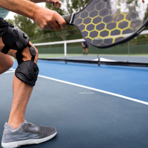Padelspieler in Bewegung mit einem Schläger und Knieorthese auf einem Tennisplatz.