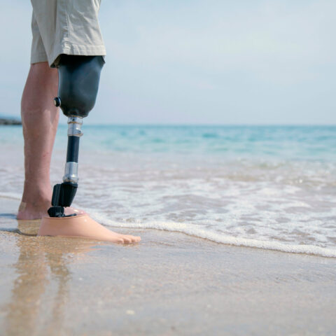 Mann mit Beinprothese, der im Wasser am Strand steht, während die Wellen sanft über seine Füße rollen.