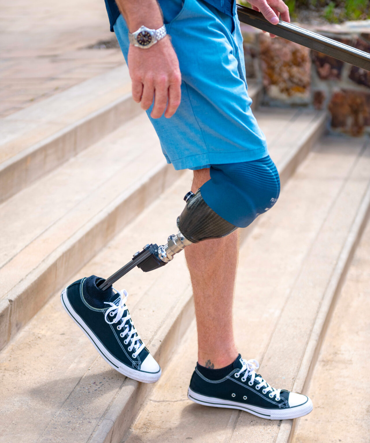 Mann mit einer Beinprothese und schwarzen Sneakers, der eine Treppe hinuntergeht.