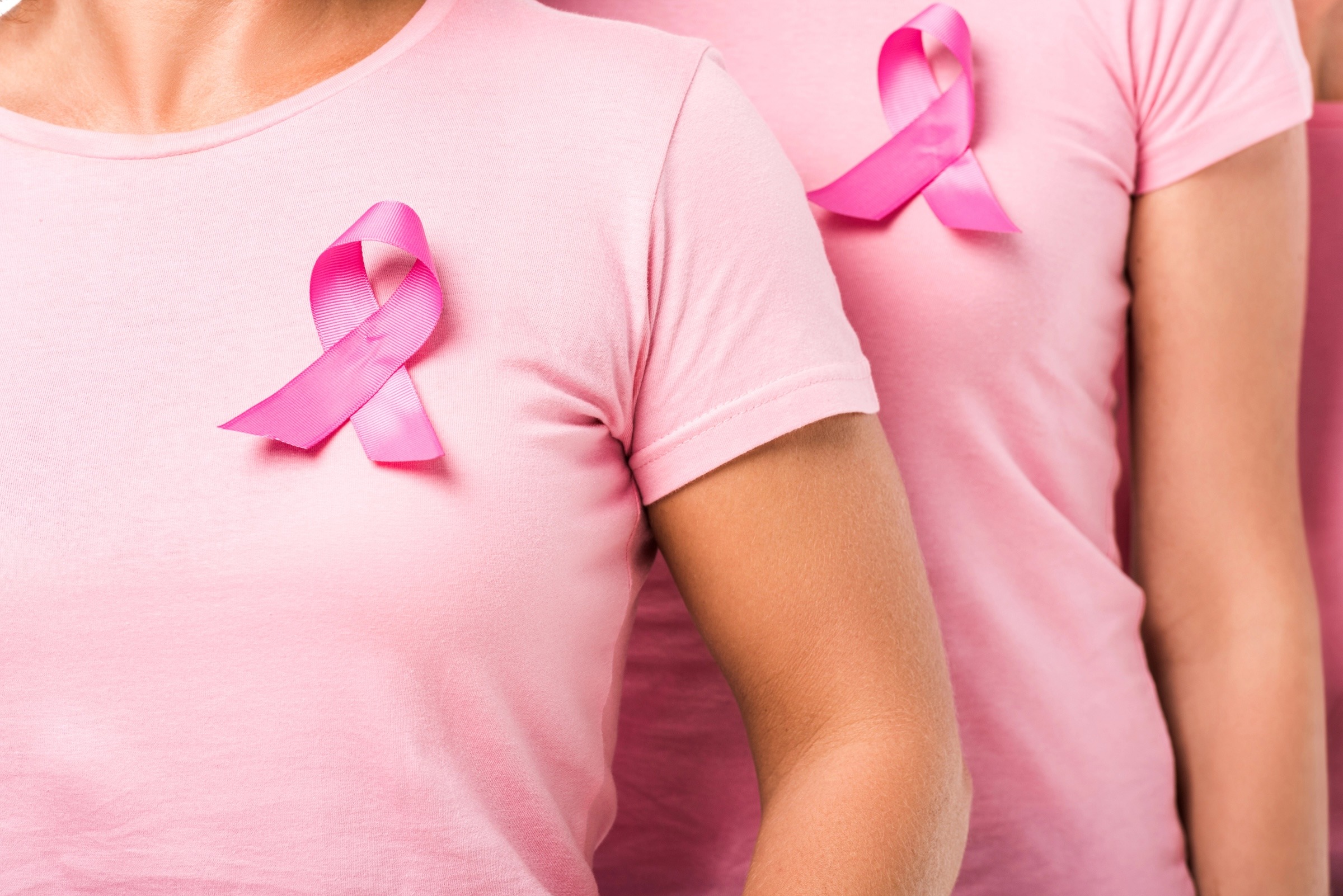 Drei Frauen in pinken T-Shirts mit pinken Ribbons auf der Brust, die für das Bewusstsein für Brustkrebs stehen.
